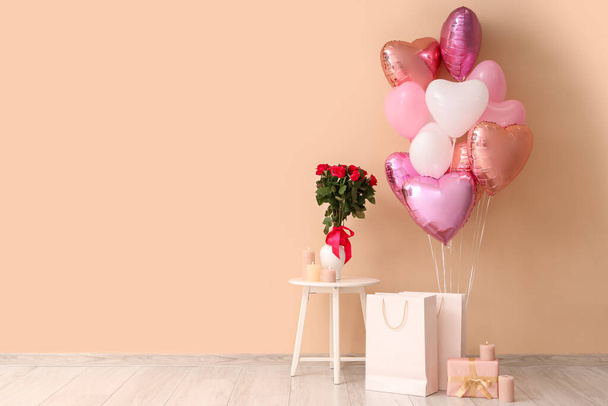 Heart-shaped balloons with shopping bags and bouquet of roses near beige wall. Valentine's Day celebration - 写真・画像