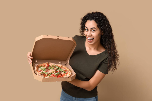 Beautiful young happy African-American woman with delicious pizza on beige background - Valokuva, kuva
