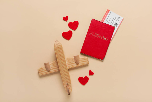 Passport with ticket, hearts and wooden airplane on beige background. Valentine's Day celebration - Photo, Image