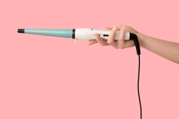 Hand of young woman with curling iron on pink background - Foto, Bild