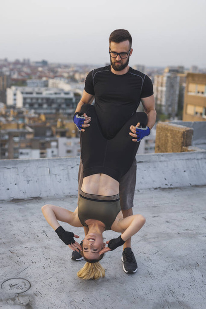 Pareja usando ropa deportiva haciendo ejercicios de crujidos colgantes en una terraza en la azotea de un edificio - Foto, Imagen