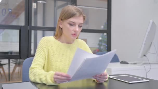 Nuori blondi nainen juhlii lukiessaan asiakirjoja - Materiaali, video