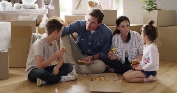 Família comendo pizza em nova casa no chão, apartamento e propriedade juntos. Imóveis, crianças famintas e pais com fast food, almoço e caixas em casa, conversa e ligação depois de se mudar para - Filmagem, Vídeo