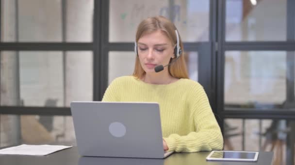 Blondýny žena se sluchátky v call centru s úsměvem na kameru - Záběry, video
