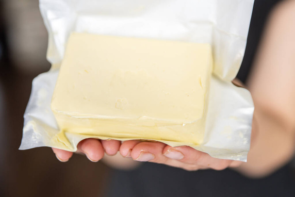 Ręka trzyma masło w opakowaniu z bliska. Proces robienia kanapek z masłem. Wysokiej jakości zdjęcie - Zdjęcie, obraz
