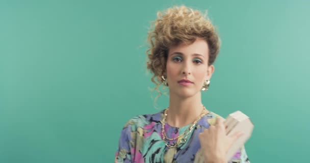 Woman, face and makeup with 80s fashion in studio for beauty on green background. Model with vintage style, mockup space and bold cosmetics in portrait with colorful clothes and funky jewelry. - Footage, Video