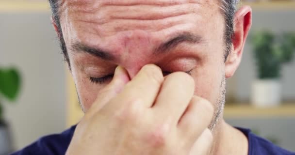 Gezicht, stress of hoofdpijn en een volwassen man close-up in zijn huis met pijn of ongemak in zijn sinus. Depressie, angst of burn-out en een persoon van middelbare leeftijd die zich moe en uitgeput voelt met vermoeidheid. - Video