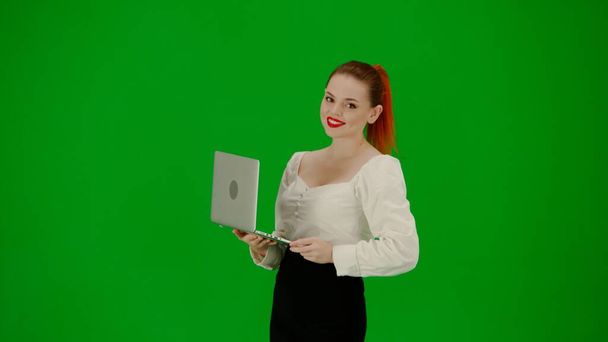 Modern business woman creative advertisement concept. Portrait of attractive office girl on chroma key green screen. Woman in skirt and blouse holding laptop and typing, positive focused expression. - Фото, зображення