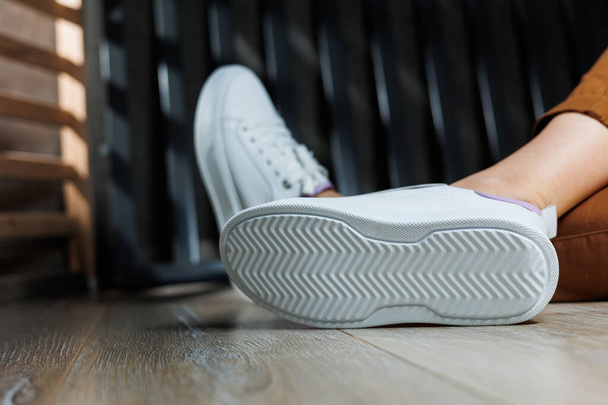 Белые кожаные кроссовки на женских ногах. Женские ноги в удобных повседневных кроссовках - Фото, изображение