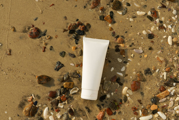 maqueta blanca de un tubo de protector solar o crema hidratante en conchas marinas y arena en la playa junto al mar. El concepto de cosméticos de verano para el bronceado y la protección corporal - Foto, Imagen