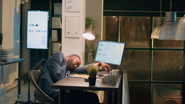 Coworker leaving work, dissaproving of employee falling asleep in desk chair overnight. Businessman finishing nightshift, dissapointed to see colleague sleeping at computer in office - Photo, Image