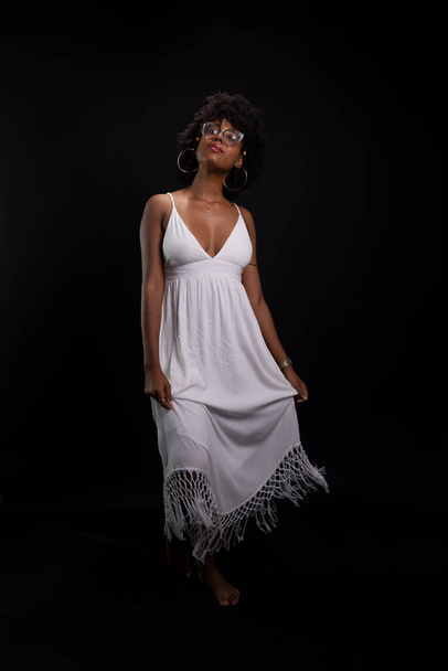 Beautiful beauty, with black power hair, standing moving her white dress against a black background. - Photo, Image