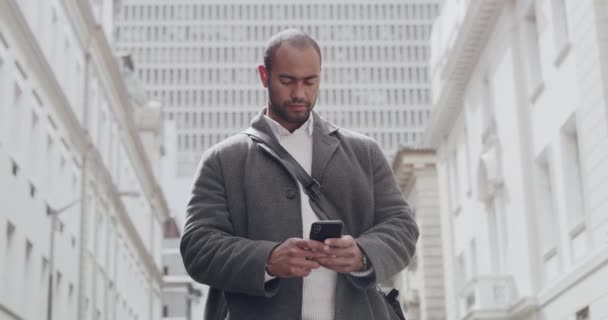 Casual man die sms 'jes leest over de telefoon, een bericht typt en sociale media controleert terwijl hij alleen in de stad staat. Serieuze zwarte man surfen op internet, chatten online en op zoek naar locatie in het centrum. - Video