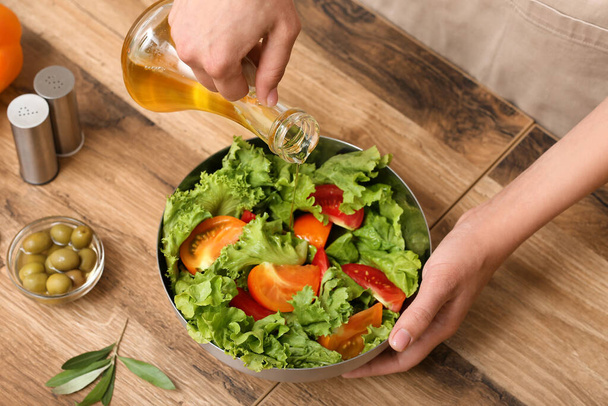 Žena přidává olivový olej do misky s chutným salátem u stolu - Fotografie, Obrázek