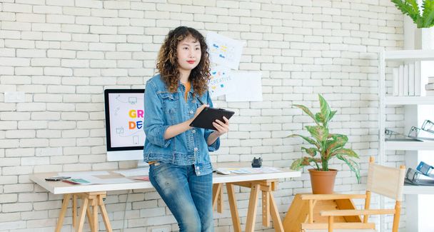 Aziatisch professioneel succesvol jong vrouwelijk creatief grafisch ontwerper in casual modieuze denim jeans jas staande lachende holding tablet computer werken in de werkruimte in het kantoor van het bedrijf. - Foto, afbeelding