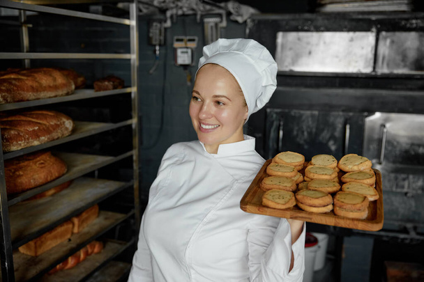 Жінка-кухар з лотком апетиту смачне тістечко, що стоїть на хлібопекарській кухні. приготування вівсяного печива - Фото, зображення