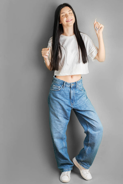 Ολόσωμο πορτραίτο μιας νεαρής έφηβης με λευκό μπλουζάκι και τζιν. - Φωτογραφία, εικόνα