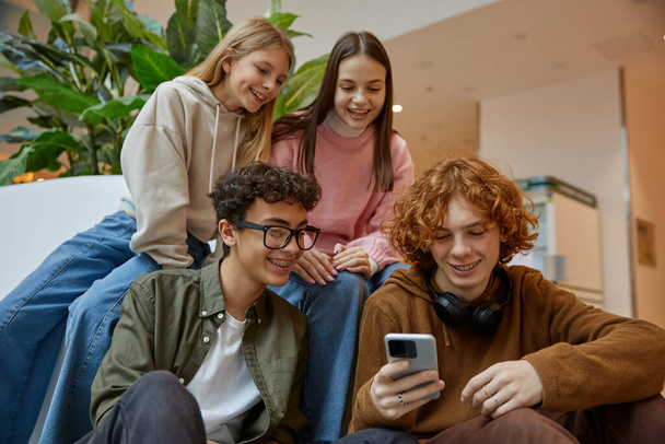 Happy teenage friends watching funny video on smartphone browsing on internet and smiling together while rest at shopping mall. Technology and friendship concept - Foto, afbeelding