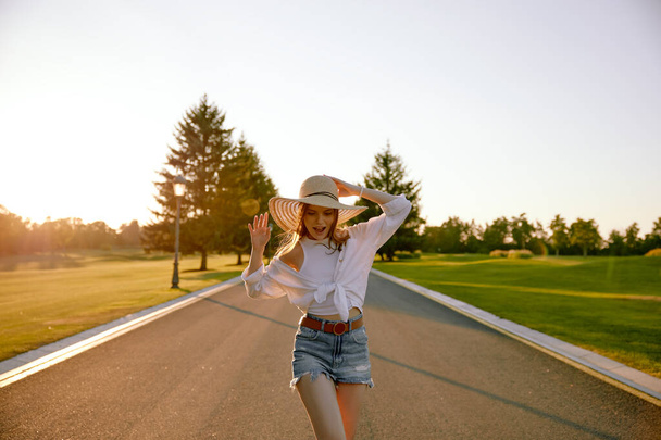Portret van charmante jonge hippe vrouw met strohoed over de weg. Reis, reis avontuur en outdoor recreatie tijd concept - Foto, afbeelding