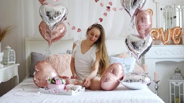 Evdeki güzel genç kız sabah yatakta kalp şeklinde balonlarla sevgililer günü kutlamasının tadını çıkarıyor. Yüksek kalite 4k görüntü - Video, Çekim