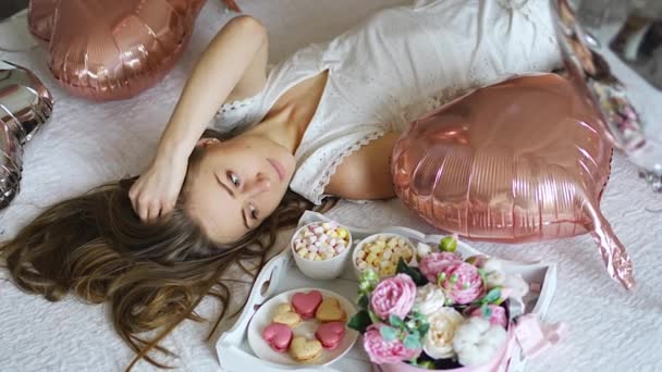 Красивая молодая девушка дома на кровати утром насладиться День Святого Валентина праздник с сердечной формы воздушные шары. Высококачественные 4k кадры - Кадры, видео