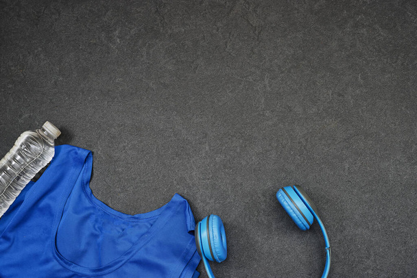 Terveellinen elämäntapa, urheilu tai urheilijan laitteet setti: naisten vaatteet ja pullo vettä sininen langaton kuuloke harmaalla pohjalla - Valokuva, kuva