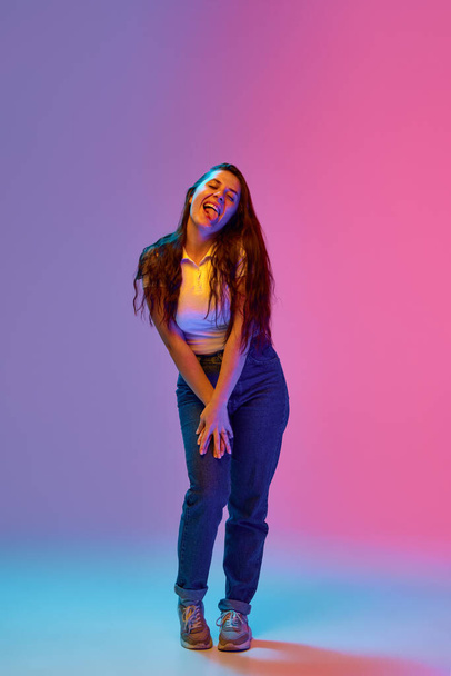 Full-length portrait of positive and funny young brunette woman with freckles grimacing against gradient background in neon light. Concept of beauty and youth, human emotions, self-expression. Ad - Foto, Bild