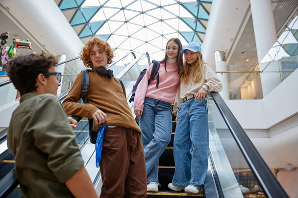 Felice squadra di amici adolescenti che spostano le scale al centro commerciale. Sorridente allegro ragazzi e ragazze in piedi sulla scala mobile - Foto, immagini