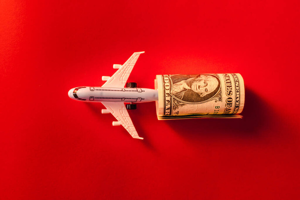 Toy airplane, twisted dollar bill, red surface.Copy space. - Photo, image