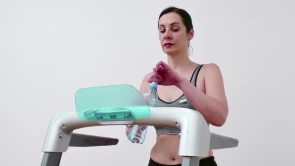 Mujer joven está haciendo ejercicio en una cinta de correr y beber agua para hidratar su cuerpo, Video Clip 4K - Imágenes, Vídeo