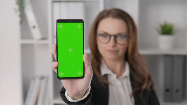 Chroma key template green screen on smartphone. Business woman holding and showing phone screen on camera in office. Competent and confident: a business analyst who helps you make informed decisions - Кадри, відео