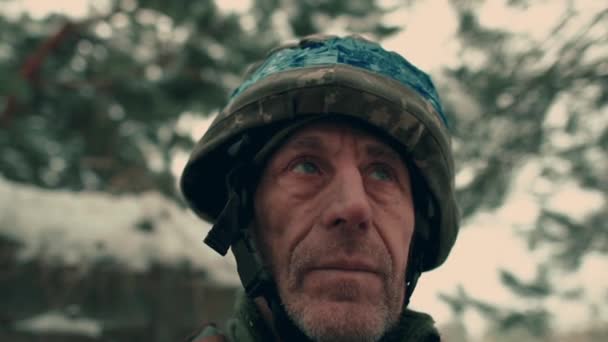 Close-up of an elderly Ukrainian soldier in military uniform and helmet. A Ukrainian soldier in a snowy trench. - Video, Çekim