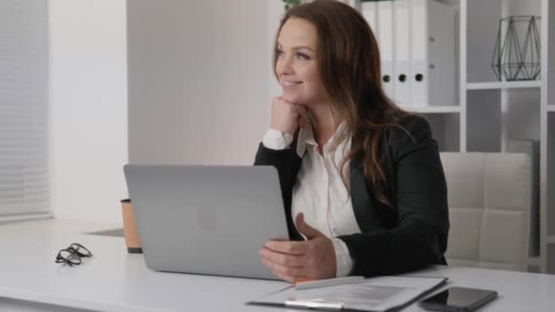 A businesswoman who turns challenges into opportunities and leads her team to victory. A successful woman smiles dreamily, happily imagines the positive results of her work. Business woman with laptop - Imágenes, Vídeo