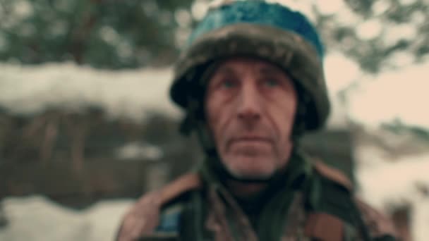 Close-up of an elderly Ukrainian soldier in military uniform and helmet. A Ukrainian soldier in a snowy trench. - Πλάνα, βίντεο