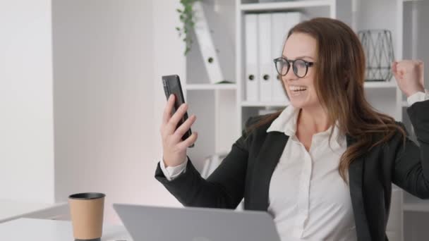 An energetic businesswoman, with a phone in her hands, confidently manages communication and solves important tasks in real time. A woman is happy looking at her phone, saw the good news and is - Кадри, відео