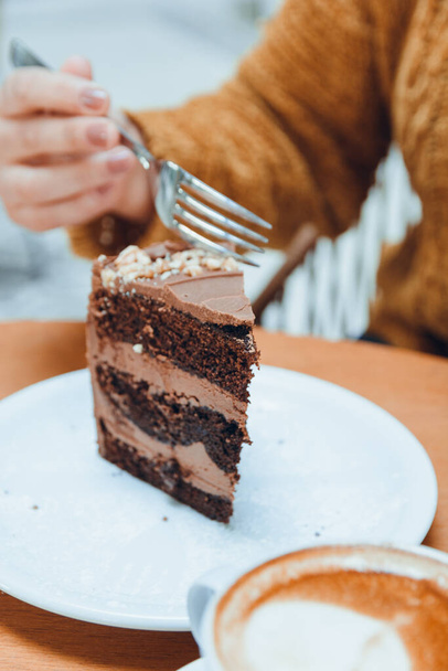 image verticale de la main d'une femme caucasienne méconnaissable coupant avec une fourchette une tranche de gâteau au chocolat servi sur une plaque de porcelaine blanche sur une table en bois, concept de pâtisserie pour les médias sociaux, espace de copie - Photo, image