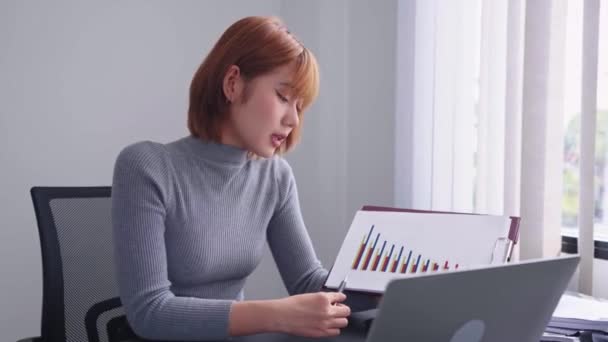 Une femme d'affaires asiatique confiante, présentant avec diligence la performance trimestrielle de l'entreprise à travers un appel vidéo déterminé sur son ordinateur portable à son espace de travail bien organisé. - Séquence, vidéo
