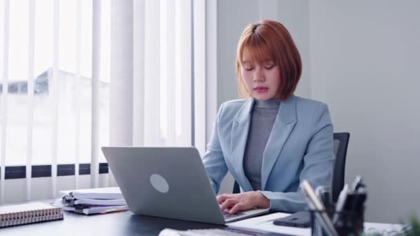 Een energieke Aziatische zakenvrouw, vol vertrouwen aan de telefoon pratend met enthousiasme, terwijl ze tegelijkertijd werkt aan haar laptop, met een bruisende en levendige houding. Hoge kwaliteit 4k beeldmateriaal - Video