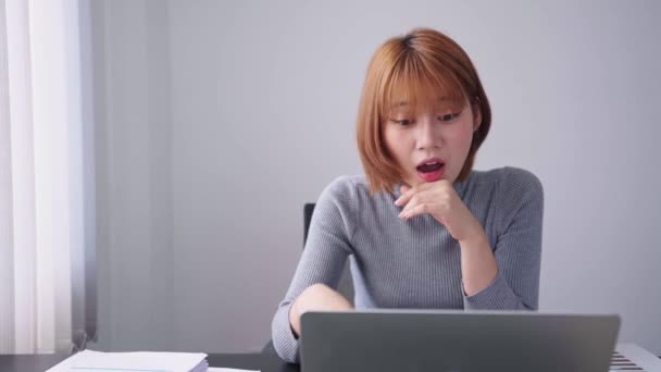 Una mujer de negocios asiática confiada, discutiendo y explicando seriamente las tareas de trabajo a sus colegas a través de una videollamada en su computadora portátil en su espacio de trabajo dedicado. - Metraje, vídeo