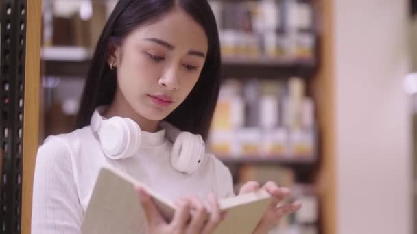 Asian Female person or student reading book sitting on floor by bookshelf in the university library, education concept - Footage, Video