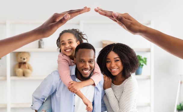 Love, Care And Support. Smiling black parents carrying their smiling preteen kid daughter, posing together at home under symbolic roof made out of hands, collage - 写真・画像
