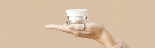A womans hand in a sweater holds a jar of cream on a beige background. Body care beauty treatment concept. - Fotó, kép