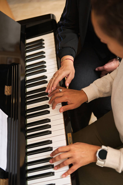 Bovenaanzicht van een jonge vrouw die piano leert spelen, pianotoetsen aanraakt onder leiding van haar leraar tijdens individuele muziekles indoor. Kunst, cultuur en amusement - Foto, afbeelding