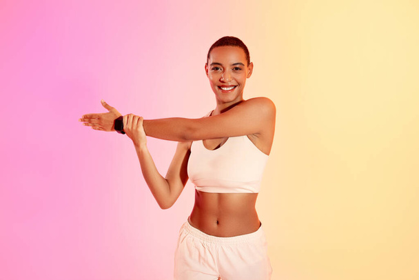 A smiling woman in sportswear checks her fitness tracker during a workout, showcasing a healthy lifestyle against a gradient pink and yellow backdrop. Fit, sport and health care - Фото, изображение