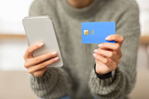 Cropped of woman using credit card and smartphone at home, paying for goods and services on Internet. Cell phone and bank card in lady hands, shopping or banking online, copy space - Foto, imagen