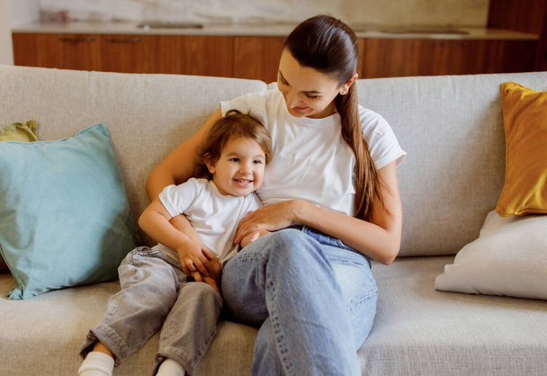 Mother And Daughter. Portrait Of Happy Loving Family Of Two Mom And Female Child Bonding Together While Sitting On Couch At Home, Young Woman And Her Kid Embracing And Smiling, Free Space - Foto, afbeelding
