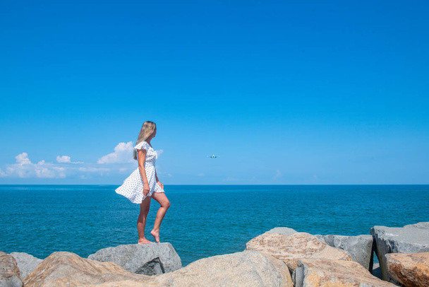 Seaside Chic: A Girl in a White Dress by the Serene Blue Sea. High quality photo - Zdjęcie, obraz