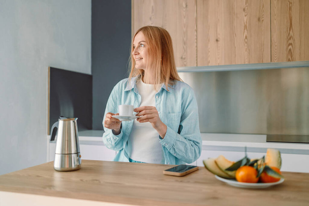 Muotokuva onnellinen nainen nauttia kupin kuumaa kahvia keittiössä ja hymyillen, nauttia viihtyisä aamu. Laadukas kuva - Valokuva, kuva