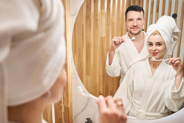 Young couple doing morning routine in bathroom, people in fluffy bathrobes - Foto, immagini