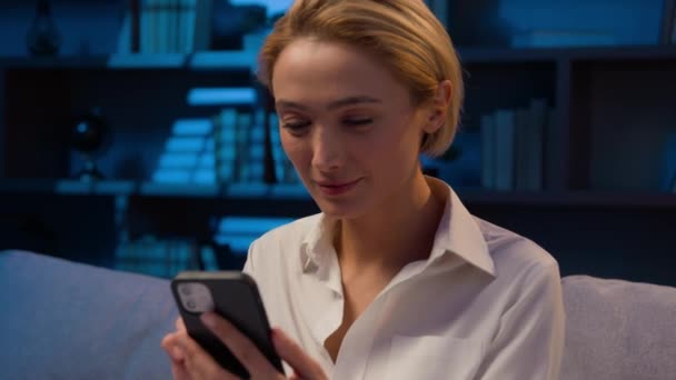 kaukaska kobieta w nocy dom biuro przewijanie telefon komórkowy social media przeglądanie usług internetowych zakupy online ze smartfonem businesswoman kobieta z telefonu uśmiechnięty ząb do kamery - Materiał filmowy, wideo